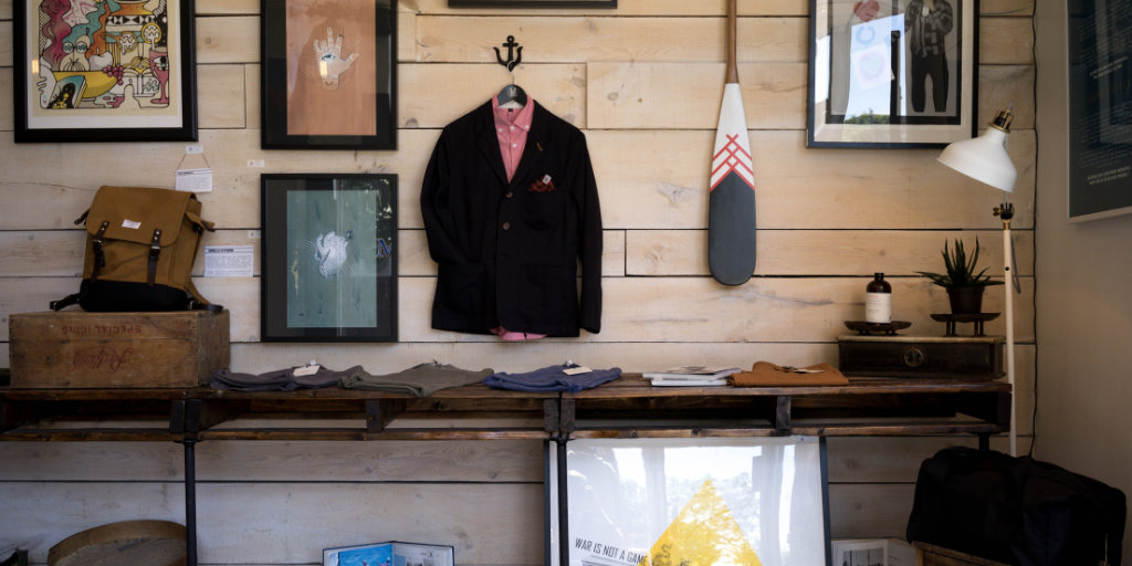 Hipster shop with wooden panels displaying a lamp, suit, and clothing for sale.